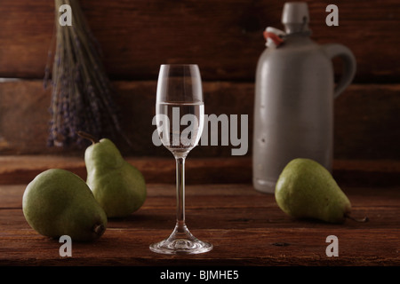 Bicchiere di acquavite di pere con pere e un vaso di whiskey su un rustico sfondo di legno Foto Stock