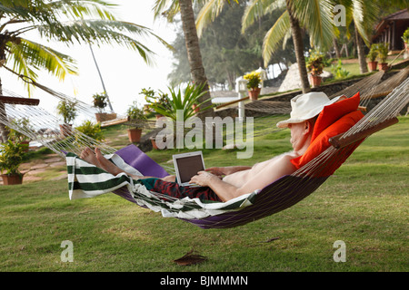 Uomo che indossa un cappello, giacente in una amaca sotto le palme e rilassarsi mentre si lavora con un netbook, Betsaida eremo vicino Kova Foto Stock