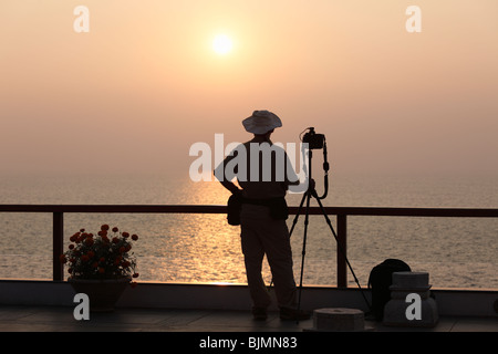 Fotografo con una telecamera su un treppiede di fronte al tramonto sul mare, Kovalam, Kerala, India meridionale, India, Asia Foto Stock