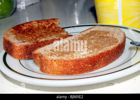 Due grosse fette di pane abbrustolito, imburrato pane integrale sulla piastra bianca accanto al contenitore di diffusione. Foto Stock
