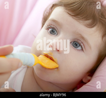 Alimentazione madre bambino cucchiaio giallo sfondo bianco Foto Stock