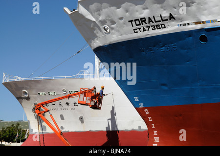 Uomo in pittura cherrypicker dello scafo di una nave da pesca in una darsena Porto di Città del Capo Sud Africa Foto Stock