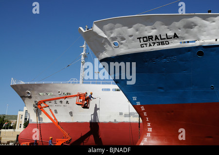 Uomo in pittura cherrypicker dello scafo di una nave da pesca in una darsena Porto di Città del Capo Sud Africa Foto Stock