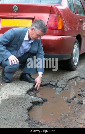 il conducente con auto rossa sta ispezionando la buca su strada causata da condizioni climatiche invernali avverse Foto Stock