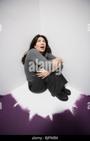 Donna seduta in un angolo cercando paura Foto Stock