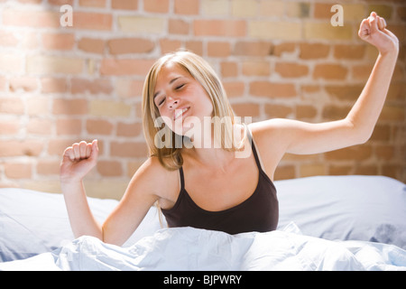 La donna a sbadigliare e stretching nel letto Foto Stock