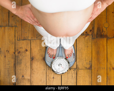 Donna incinta in piedi sulla bilancia Foto Stock