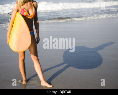 Giovane donna con la tavola da surf in spiaggia Foto Stock