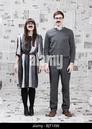 Due giovani con baffi finti in piedi in quotidiani coperto, camera studio shot Foto Stock