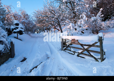 Crepuscolo cadere sulla neve invernale e la via alla carità fattoria nel villaggio Costwold di Stanton, Gloucestershire Foto Stock