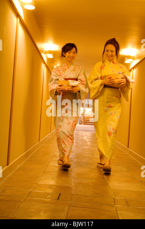 Donne che indossano yukata camminando per un corridoio di un centro termale che trasportano i prodotti spa in cestelli di bambù Foto Stock