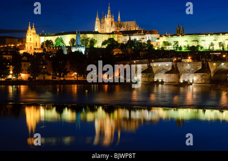 PRAGA, Repubblica Ceca - il Castello di Praga si riflette sul fiume Moldava con il Ponte Carlo sulla destra. L'iconico Castello di Praga, simbolo della storia e del potere della Repubblica Ceca, sorge maestosamente su una collina che domina la città. È il castello antico più grande del mondo e un sito patrimonio dell'umanità dell'UNESCO, che attira ogni anno innumerevoli visitatori per esplorare la sua affascinante storia e la sua diversità architettonica. Foto Stock