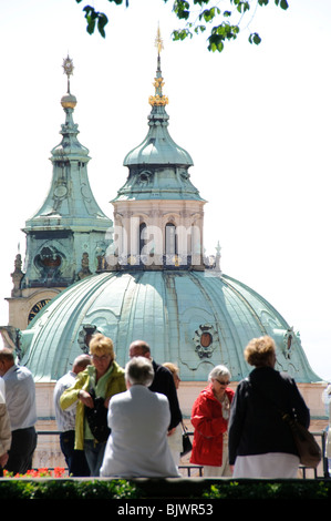 Chiesa di San Nicola città minore dal Castello di Praga Praga Praga Repubblica Ceca // PRAGA, Repubblica Ceca - la caratteristica cupola verde in rame e il campanile della Chiesa di San Nicola (Kostel svatého Mikuláše) si innalzano sopra i tetti della città minore di Praga (Malá strana). Ampiamente considerata un capolavoro dell'architettura alto barocca, la chiesa fu costruita tra il 1704 e il 1755, con Christoph Dientzenhofer e suo figlio, Kilian Ignaz Dientzenhofer, come architetti principali. L'imponente cupola ha un diametro esterno di 20 metri (66 piedi). I turisti in primo piano si possono ammirare godendosi la vista da una e Foto Stock