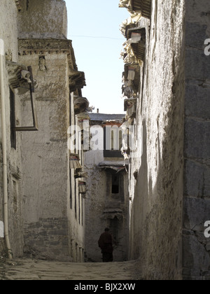 Un monaco buddista passeggiate lungo il viale tra due edifici presso il monastero di Drepung a Lhasa, in Tibet Foto Stock