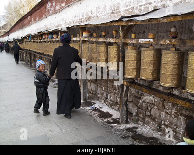 Un ragazzino guarda indietro come sua madre gira le ruote della preghiera al di fuori del palazzo del Potala a Lhasa, in Tibet Foto Stock