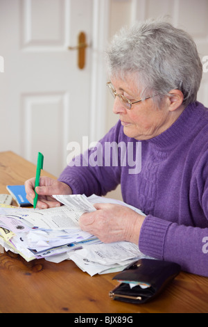 Senior donna titolare di pensione o di rendita OAP lady a casa con un sacco di fatture con la tabella di controllo di un estratto conto della carta di credito contro ricevuta. Regno Unito Gran Bretagna Foto Stock