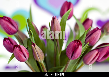 Un vaso di tulipani viola davanti a uno sfondo colorato decorato con un modello cuore Foto Stock