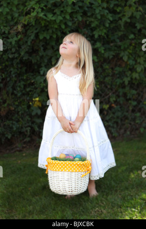 Sweet Little Girl Cerca l azienda Cesto di Pasqua con le uova in un bianco Abito in pizzo Foto Stock