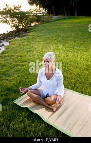 Di mezza età donna seduta sul tappeto a praticare yoga all'aperto Foto Stock