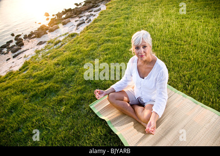 Di mezza età donna seduta sul tappeto a praticare yoga all'aperto Foto Stock