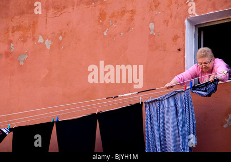 Donna appendere fuori la sua lavare da finestra a Burano, Italia Foto Stock