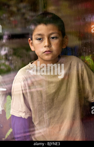 Multicultural multi-culturale di bambino 9 -10 anni vecchio ragazzo ispanico guardando fuori attraverso una finestra in un giorno di pioggia. Signor © Myrleen Pearson Foto Stock