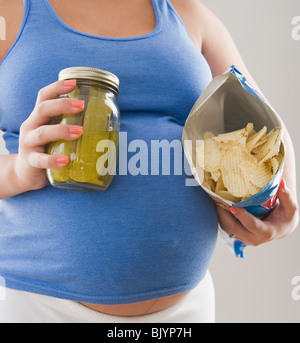 Incinta donna ispanica holding sottaceti e patate fritte Foto Stock