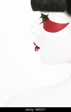 Una ragazza giapponese in Geisha make-up il profilo laterale di close-up colpo alla testa. Elevato La chiave studio fotografico. I capelli neri di colore rosso e bianco per il make-up Foto Stock