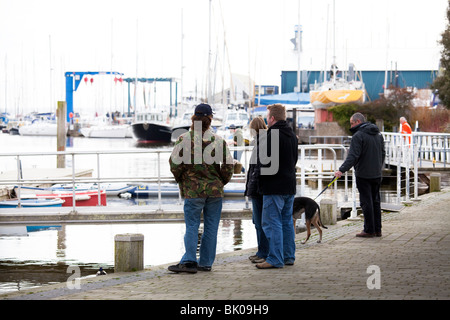 Un gruppo di persone e di un uomo con un cane in una domenica mattina a piedi lungo la banchina Lymingtom Marina Foto Stock