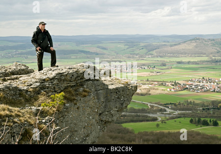 L'uomo con la fotocamera sul promontorio roccioso sulla collina Staffelberg, affacciato sul fiume Valle principale, Staffelstein, Franconia, Baviera, Germania. Foto Stock