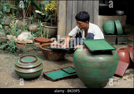 Giovane uomo l'applicazione di smalto verde al vasellame e oggetti laccati, come lui fuma un sigaro, Myanmar Foto Stock