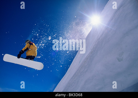 L'uomo volare attraverso l'aria su uno scarpone da snowboard con il sole sulla sua spalla in Wasatch Mountains del nord dello Utah. Foto Stock