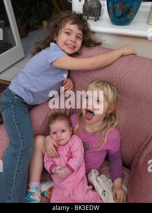 Tre sorelle di 6 e 4 anni e 2 mesi di età bambino seduto su una sedia di ridere Foto Stock