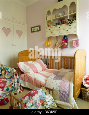 Ripiani di crema sulla parete sopra piccola culla di legno-letto con mosaico e striato biancheria da letto in Camera bambino Foto Stock