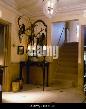 Corna di cervo sulla parete nella sala del paese con specchio sopra le lampade accese sul tavolo console Foto Stock