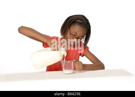 Dieci anni di vecchia ragazza versare il latte in un bicchiere coppa di misurazione. Foto Stock