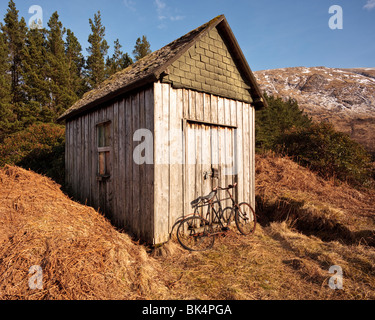 Un vecchio arrugginito bicicletta rotto appoggiato su di un capannone porta. Foto Stock