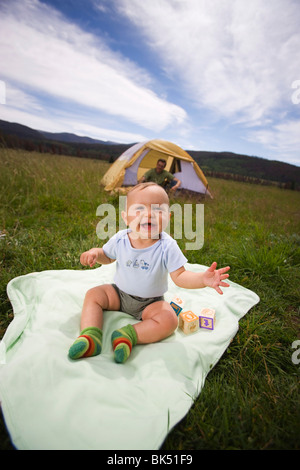 Baby sitting su una coperta all'aperto, Padre in una tenda in background, Steamboat Springs, Routt County, Colorado, STATI UNITI D'AMERICA Foto Stock