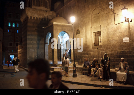 Persone a notte al di fuori di una vecchia moschea di Sana'a, Yemen Foto Stock