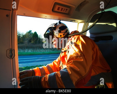 Air Ambulance paramedico guardando fuori di elicottero di porte laterali durante lo sbarco sulla scena di un incidente di automobile Foto Stock