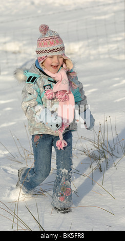 Un bambino di 5 anni Ragazza che corre nella neve divertimento sotto il cielo blu nel Lake District inglese Foto Stock