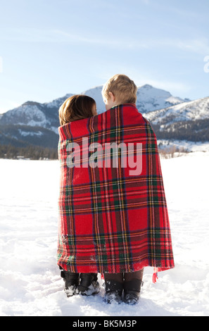 Un ragazzo e una ragazza avvolto in rosso plaid coperta nella neve Foto Stock