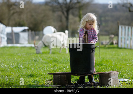 Foto di stock di un 4 anno di età bambino che gioca a streghe in giardino, agitando il suo calderone. Foto Stock