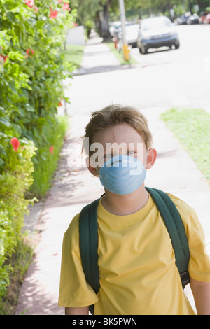 Little Boy andare a scuola a piedi che indossa una maschera per il viso Foto Stock