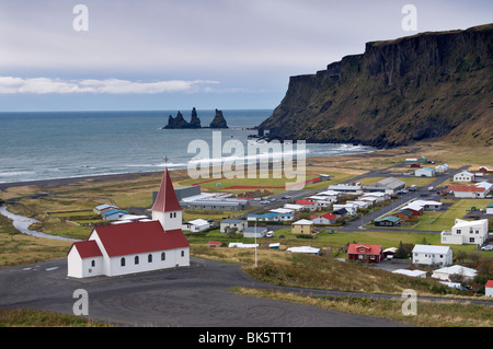 La chiesa, villaggio di Vik (Vik un Myrdal) e mare Reynisdrangar pile in distanza, Islanda, regioni polari Foto Stock