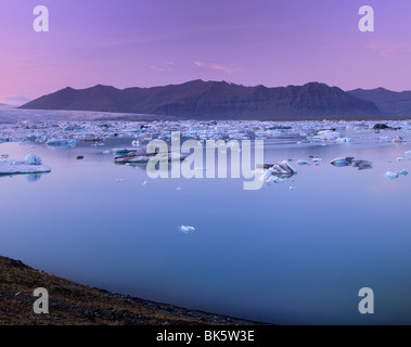 Iceberg di Jokulsarlon laguna glaciale, al tramonto, Breidamerkurjokull (Vatnajokull) ghiacciaio in distanza, Islanda Foto Stock
