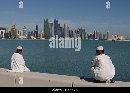 Due uomini arabi seduti sul muro con il West Bay skyline di Doha in background. Foto Stock