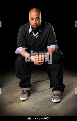 Ritratto di giovane americano africano uomo seduto con baseball hat in ginocchio Foto Stock