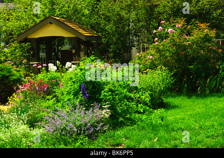 Verde e lussureggiante giardino con fiori e gazebo Foto Stock