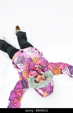 Felice ragazza adolescente rendendo angelo di neve in inverno Foto Stock